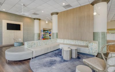 A modern lounge area with a curved sofa, round tables, chairs, and a circular rug, set against a backdrop of decorative columns.