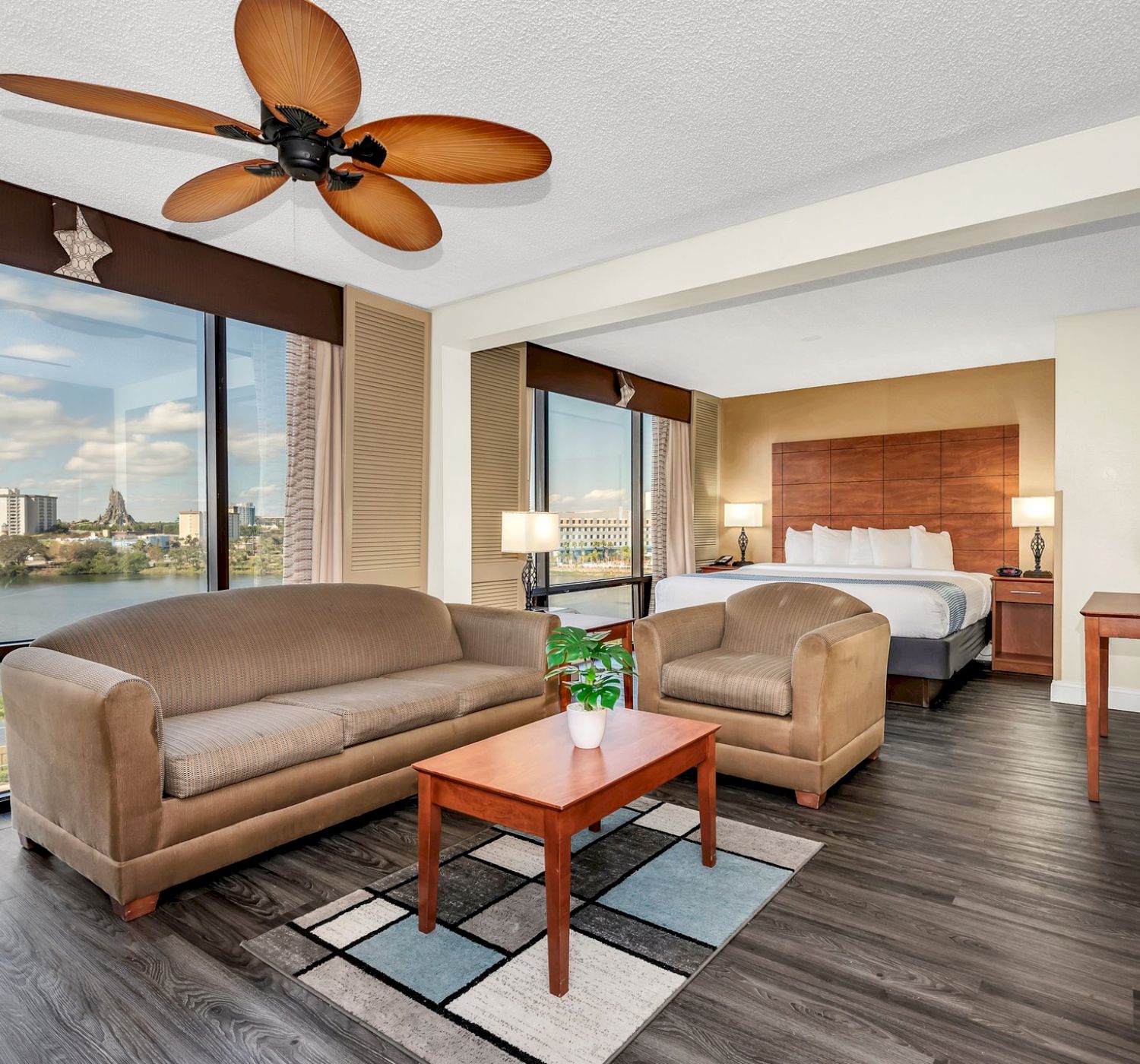 A modern hotel room with a seating area, bed, and large windows offers a view of the city and water.