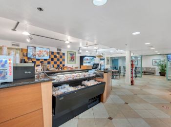 This image shows the interior of a cafe or small restaurant with a counter and various food items on display. There are tables and chairs in the background.