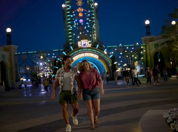 A couple walks in front of an illuminated entrance with "Epic" written above, set against a nighttime backdrop filled with lights.