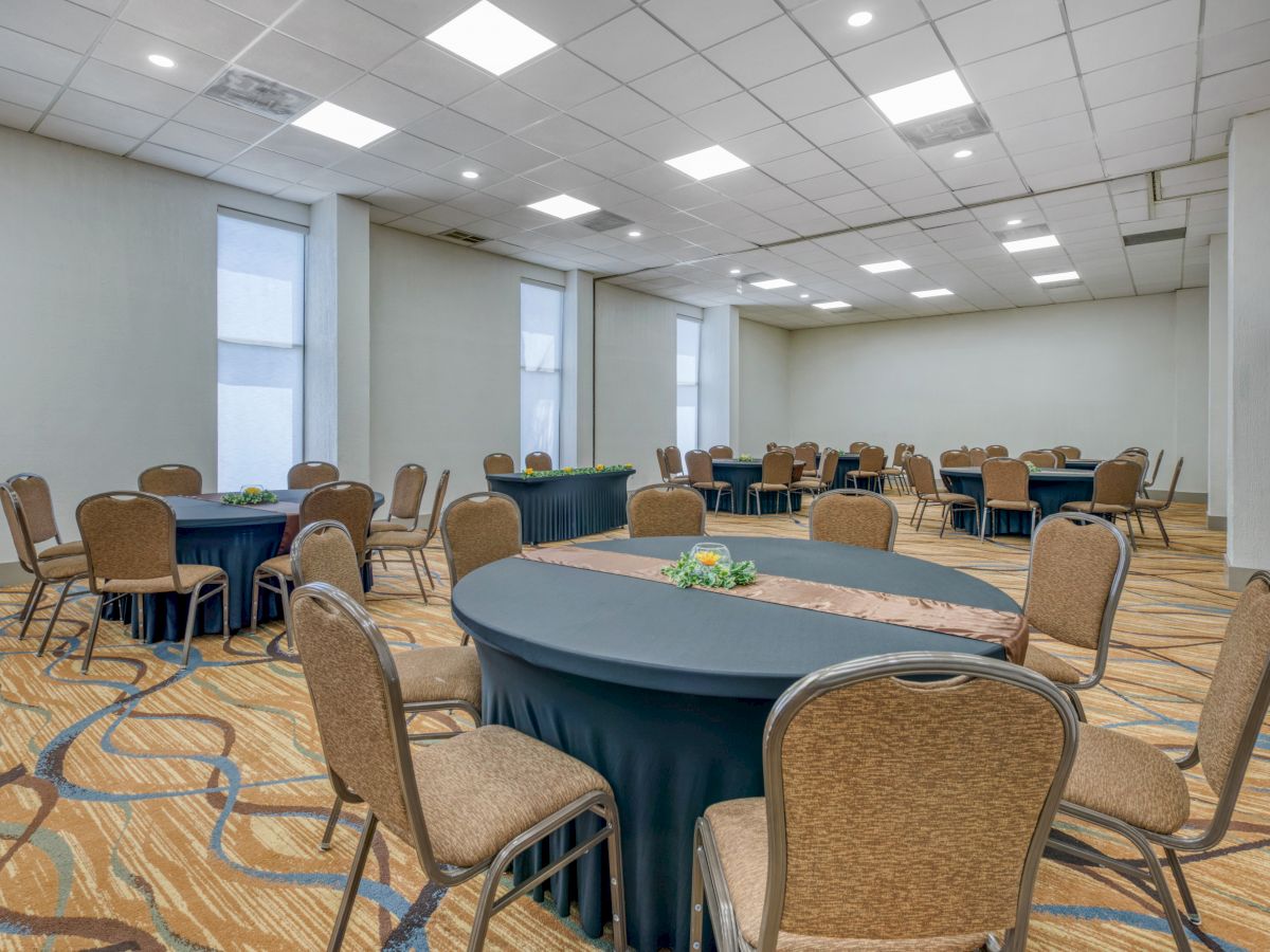 A conference room with round tables and chairs arranged for an event, featuring a patterned carpet and a white ceiling.