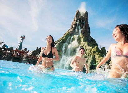 People enjoying a waterpark with a large volcano-like structure and blue sky in the background, creating a fun and lively atmosphere.