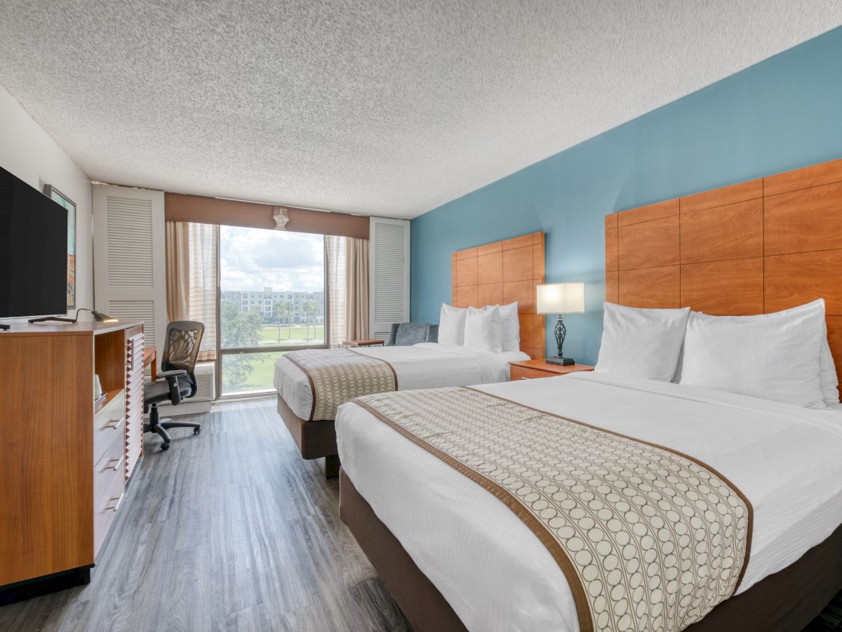 A hotel room with two beds, TV, chair, desk, and a large window overlooking greenery, featuring a modern and clean design.