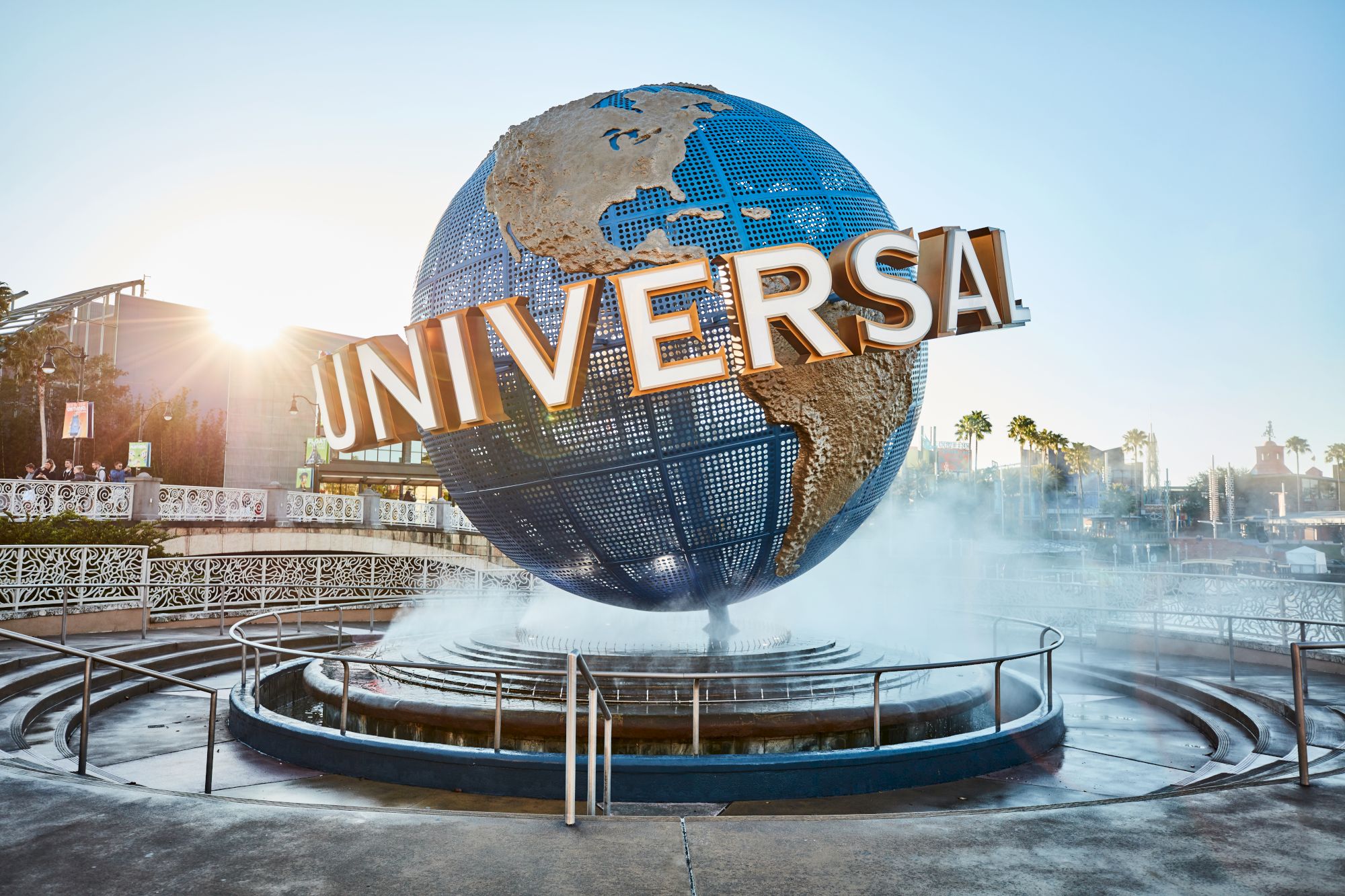 A large globe structure with "Universal" written on it, surrounded by mist and a fountain, likely at Universal Studios theme park.