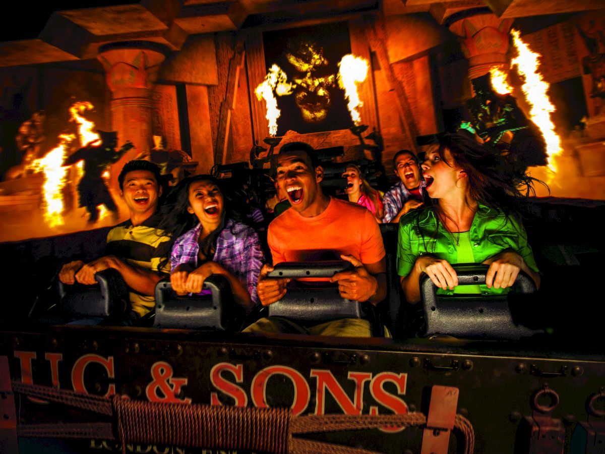 People are on a thrilling amusement park ride with fire effects and ancient temple decor, expressing excitement and fear.