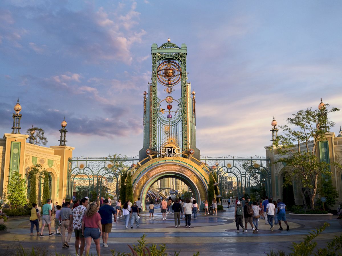 People walking towards a grand entrance with ornate architecture and a tall clock tower under a partly cloudy sky.