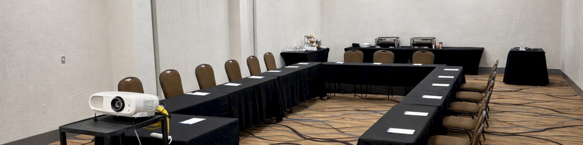 A conference room with a U-shaped table setup, a projector on a cart, and notepads on tables.