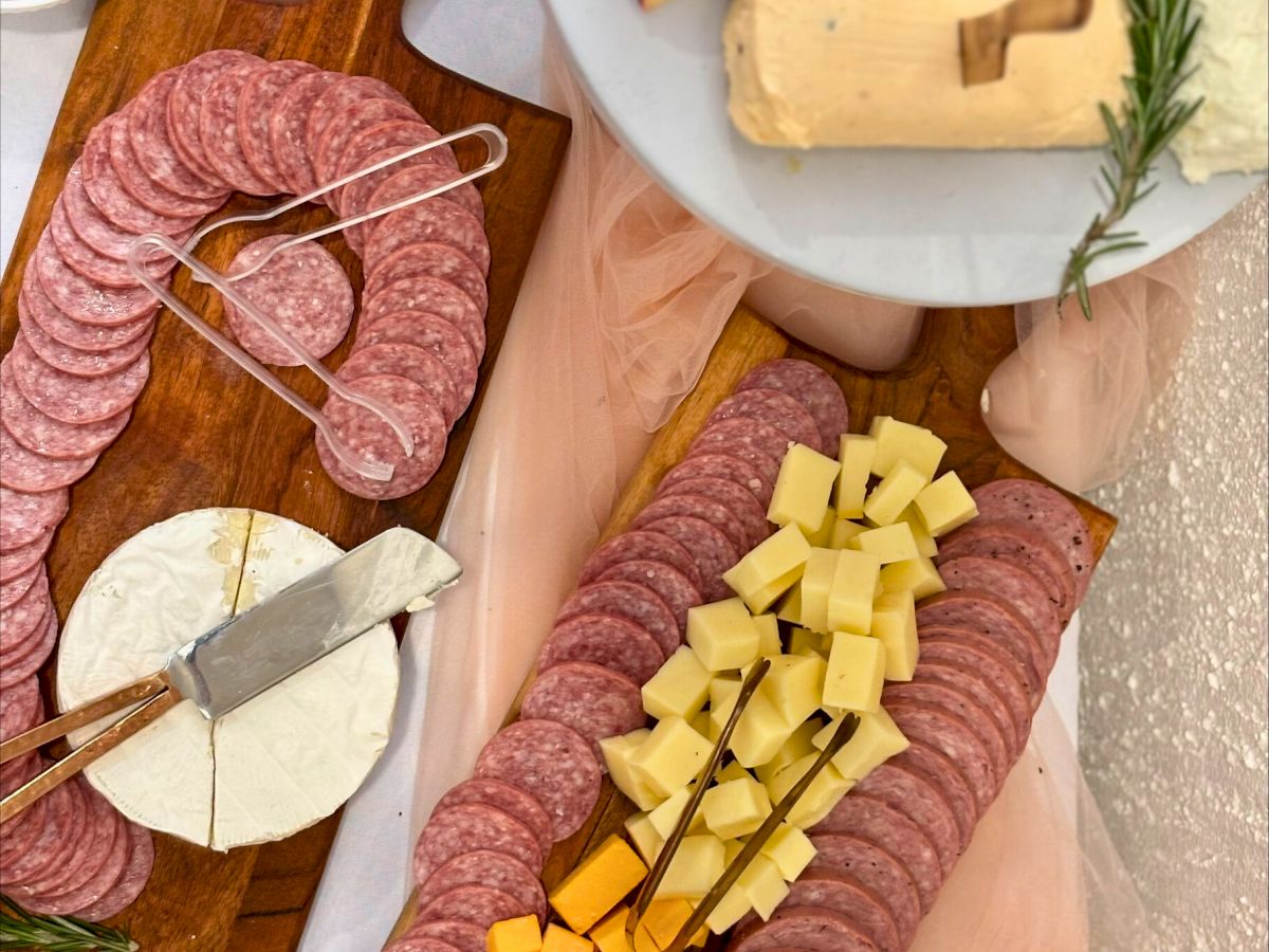 A charcuterie board with sliced meats, cheeses, crackers, grapes, and bread on wooden boards and a marble platter.