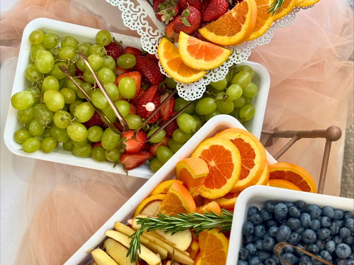 A variety of fruits are arranged on trays, including grapes, strawberries, orange slices, apple slices, and blueberries.