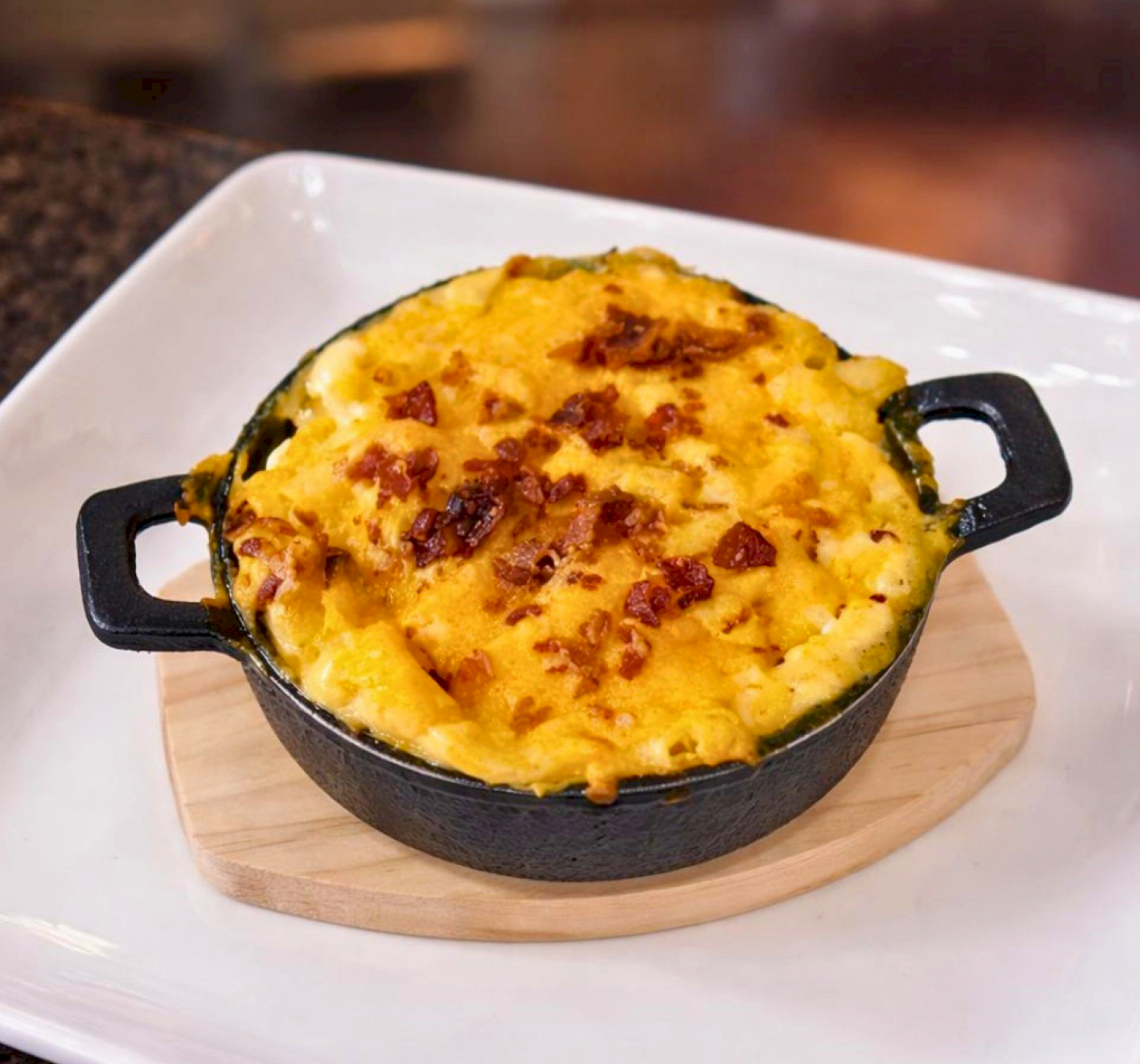A dish of baked mac and cheese in a small, round cast iron pan, topped with melted cheese and breadcrumbs.