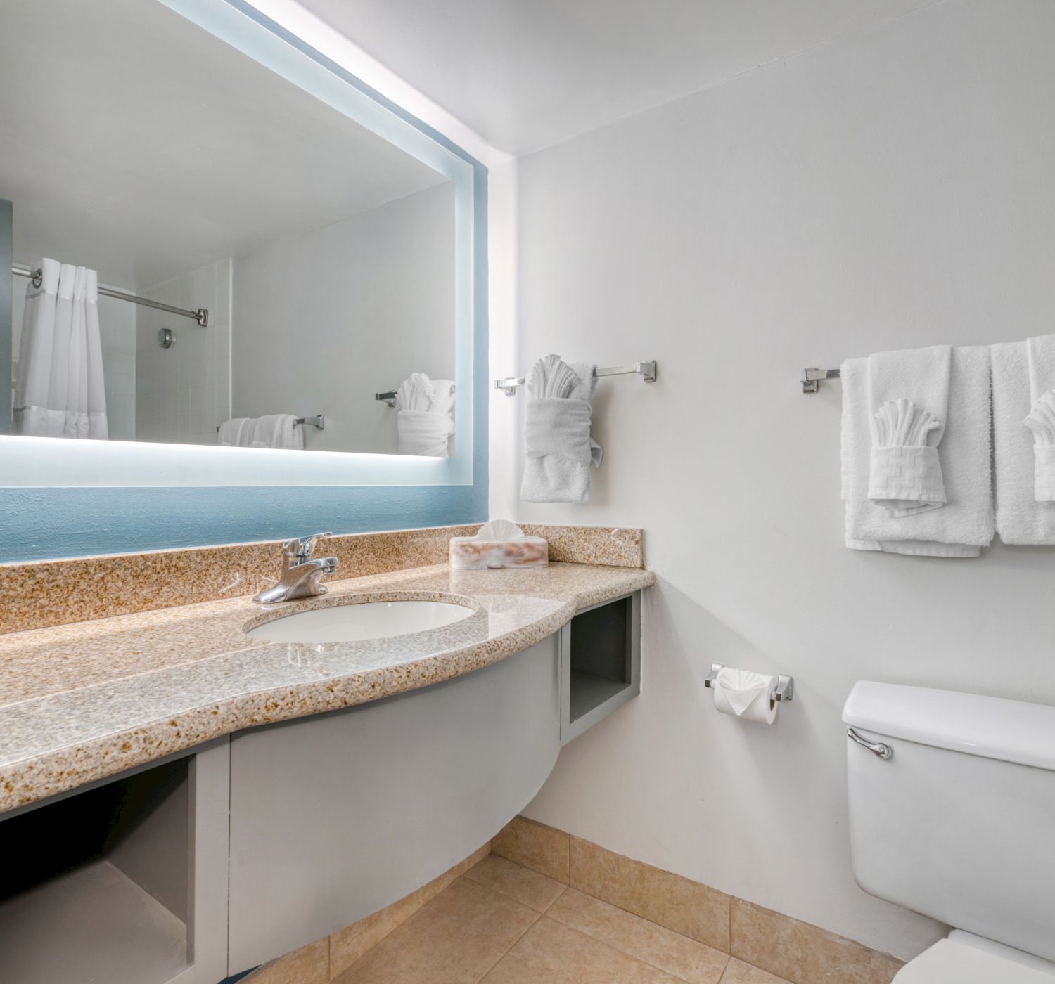 The image shows a modern bathroom with a large mirror, granite countertop, sink, towels on the rack, and a toilet.
