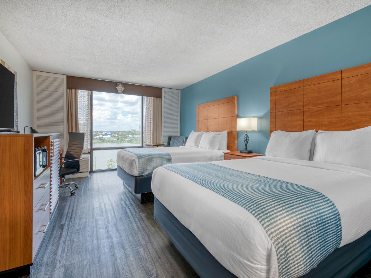 The image shows a hotel room with two beds, a TV, a desk, a window view, and chic decor in soft wood and blue tones.