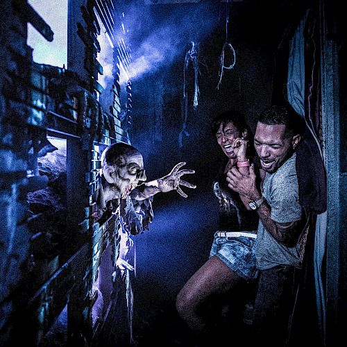 Two scared people are being startled by a creepy, zombie-like figure reaching through a broken wall in a dark, eerie setting.