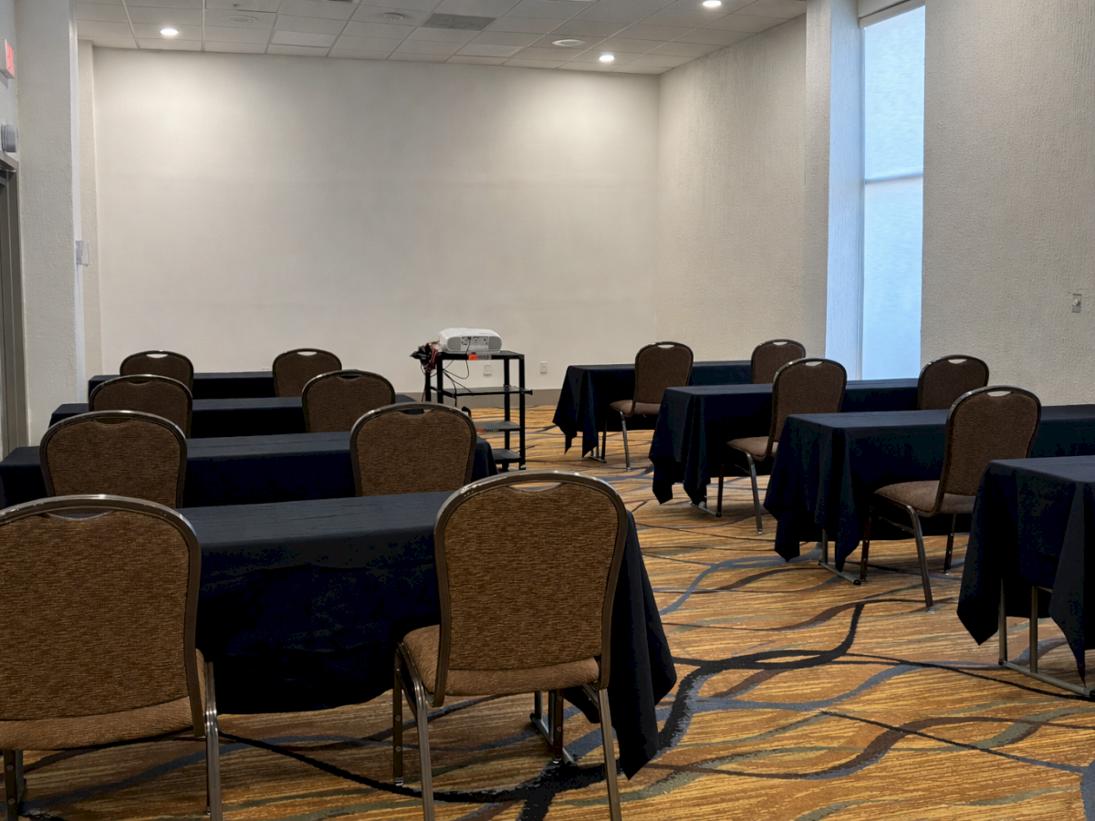The image shows a conference room with several tables and chairs arranged in rows, and a projector on a stand at the front.