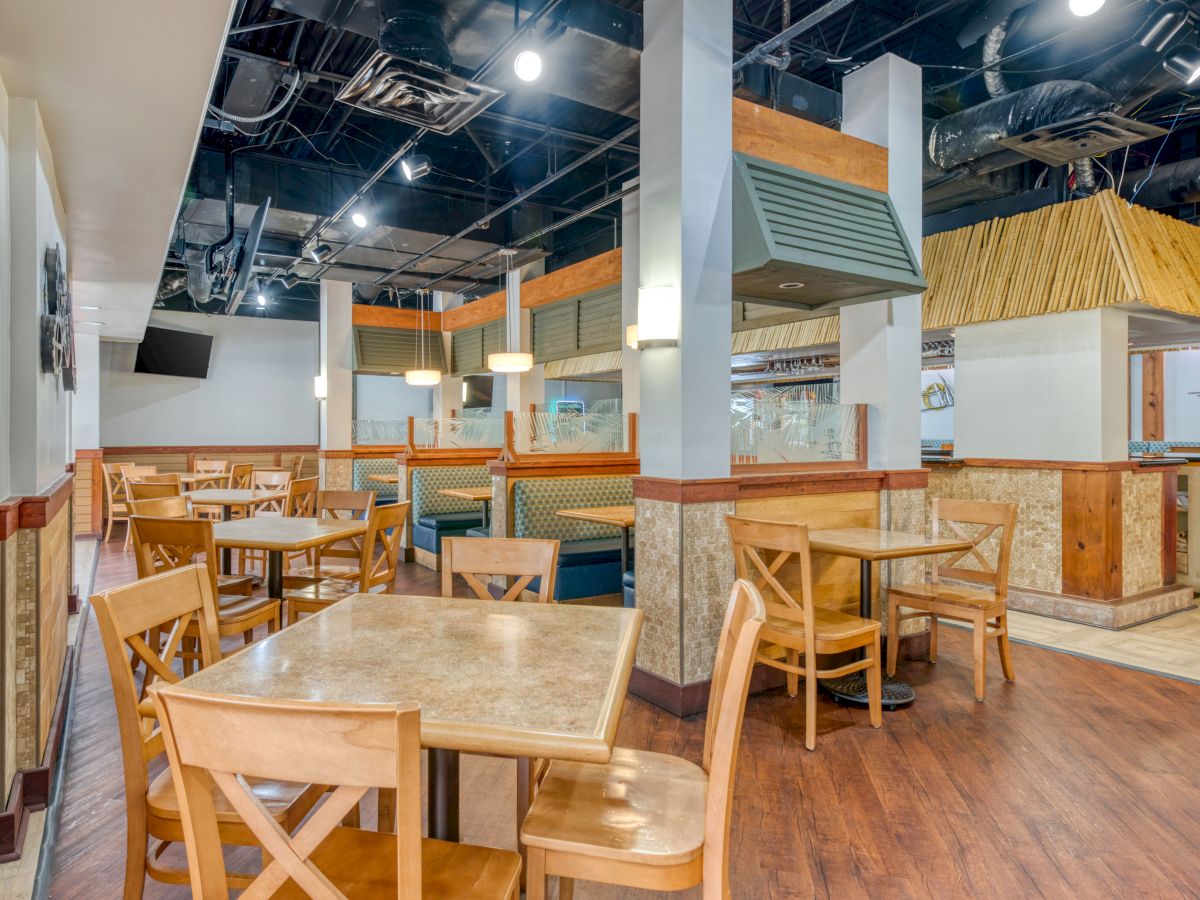 The image shows an empty restaurant with wooden tables and chairs, booths, and overhead lighting. The interior has a modern design.