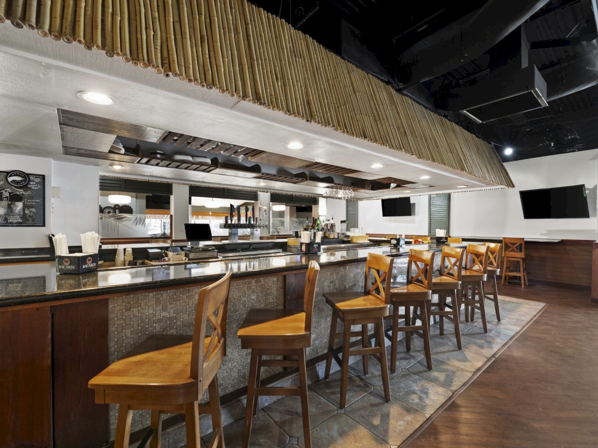 The image shows a modern bar with wooden stools, a sleek countertop, and multiple TVs in a stylish, well-lit interior.