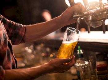 Someone is pouring a glass of beer from a tap at a bar or pub, with a warm, dimly lit atmosphere.