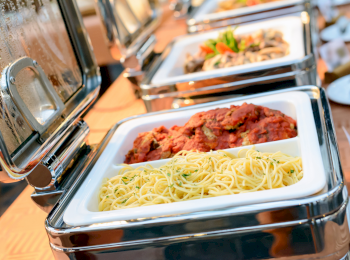 A buffet setup with a tray containing spaghetti and meatballs in tomato sauce is displayed, ready to be served.